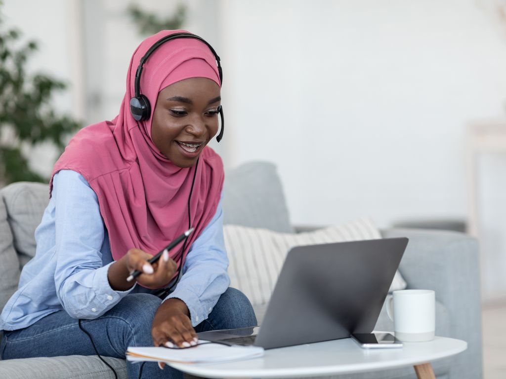 Woman in a hijab and work headset typing on a laptop