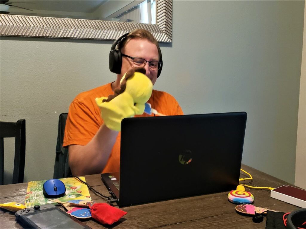 David using his digital nomad skills as an online teacher to make an online class interactive with a yellow dinosaur puppet.