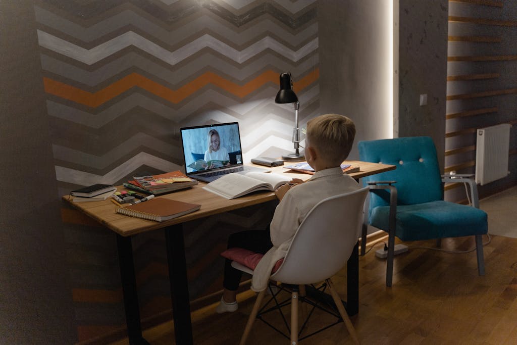 Boy sitting at a desk with a lamp lit on it while attending an online class.