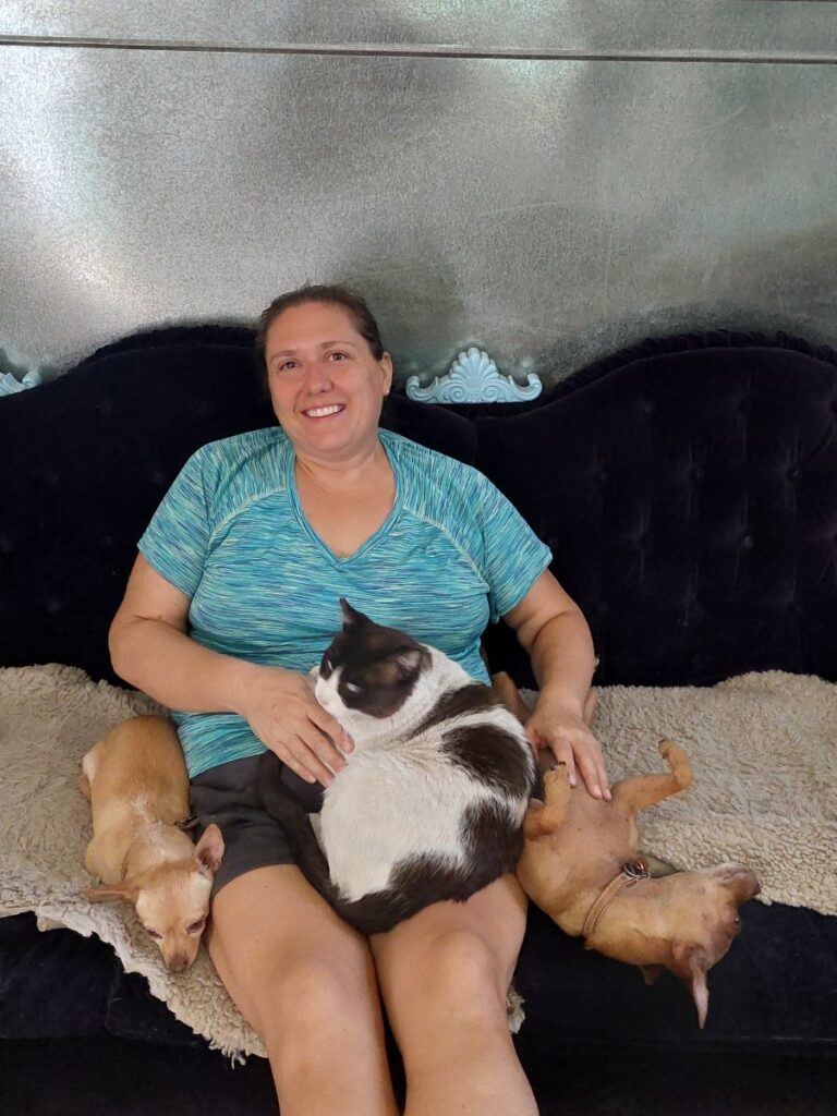 Me sitting on a couch at a house sit with two dogs and a cat laying next to or on me.